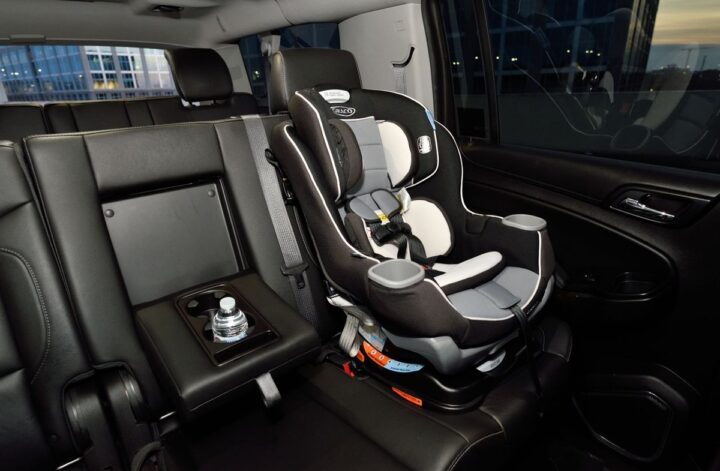 Black-and-grey child car seat with a five-point harness installed on a black leather rear vehicle seat