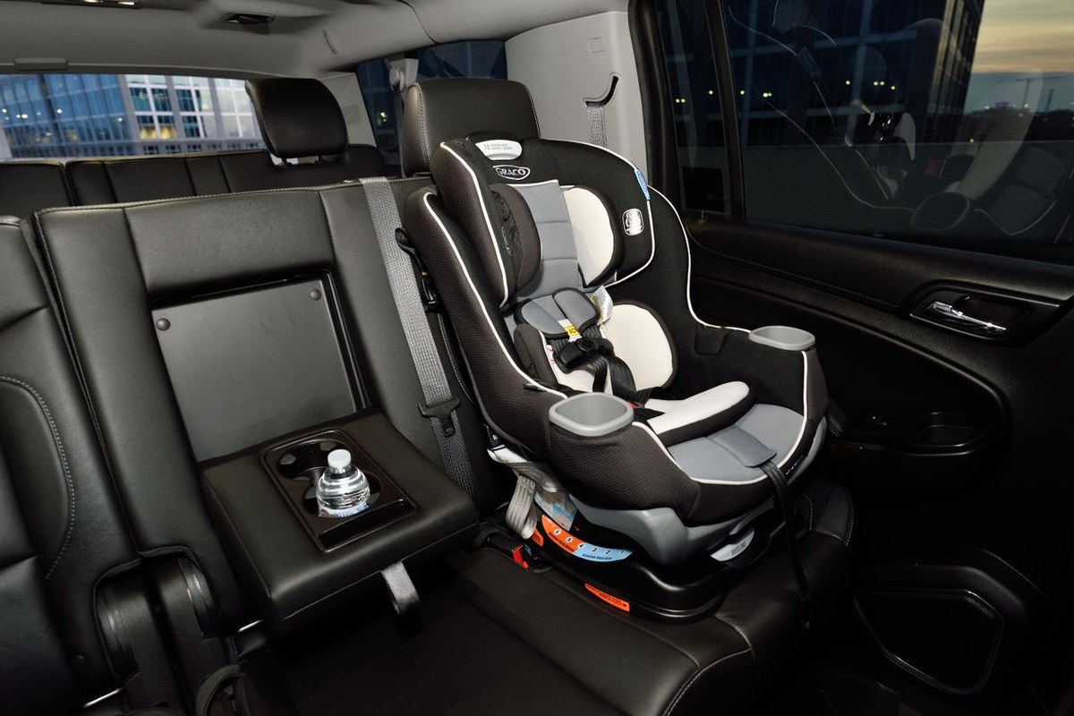 Black-and-grey child car seat with a five-point harness installed on a black leather rear vehicle seat