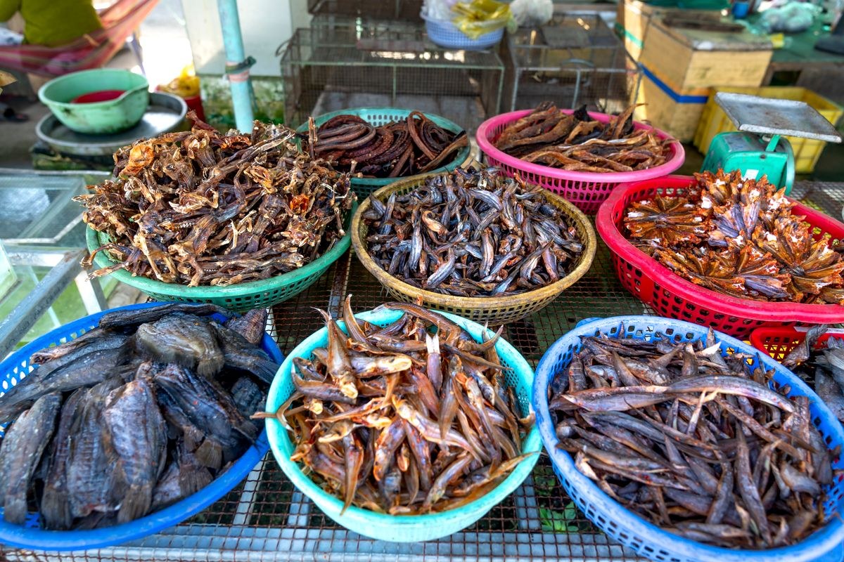 Assorted dried fish displayed in colorful plastic baskets at an outdoor market