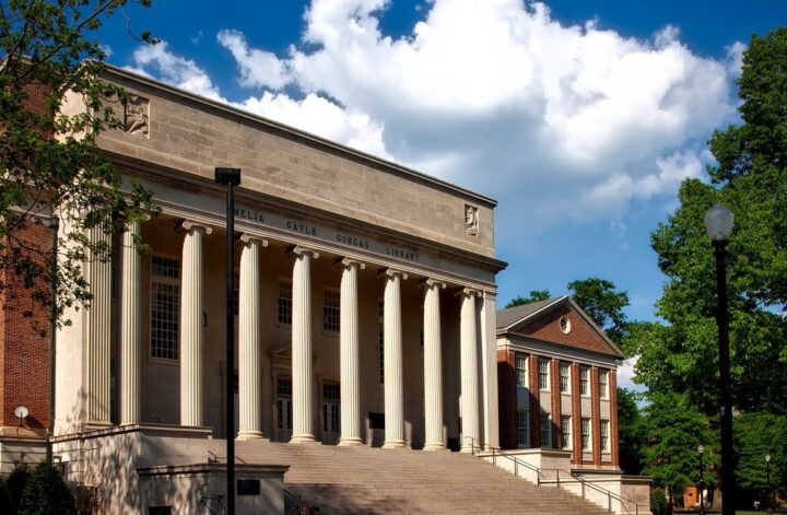 Columned neoclassical university building with wide front steps and a lawn under a blue sky