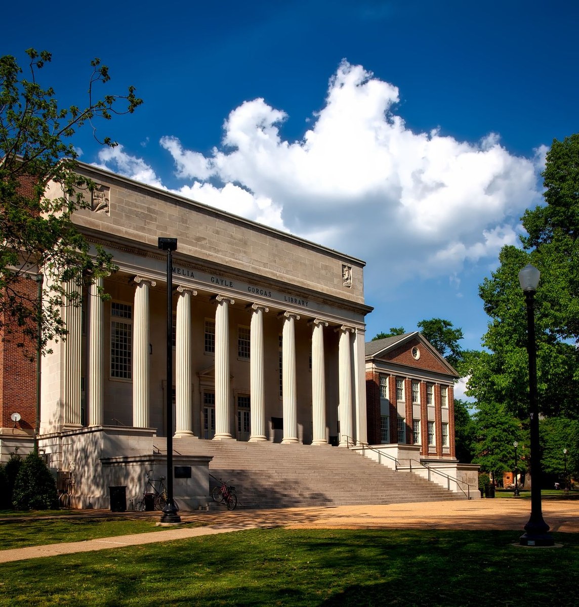 Columned neoclassical university building with wide front steps and a lawn under a blue sky